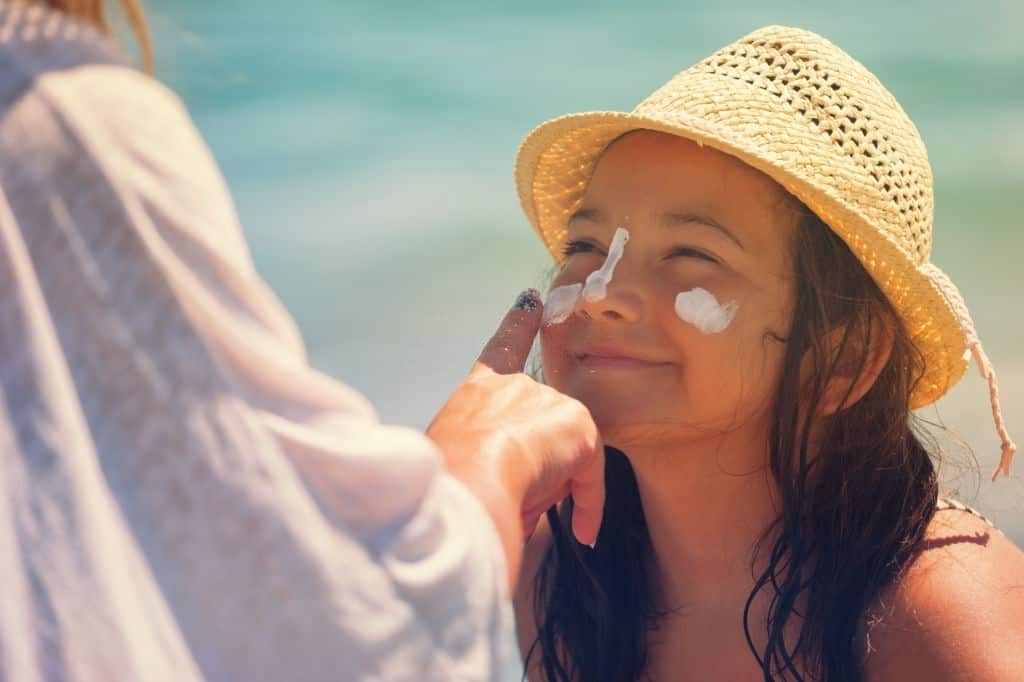 Young mother applying suntan lotion on daughter's face