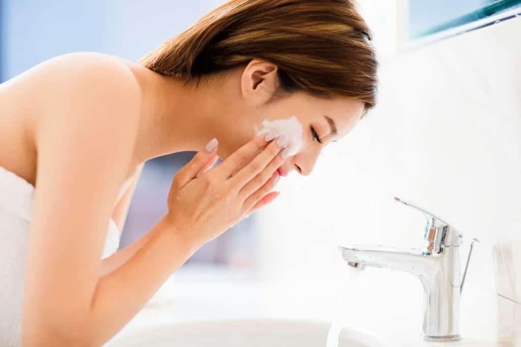 Young woman washing face with clean water in bathroom